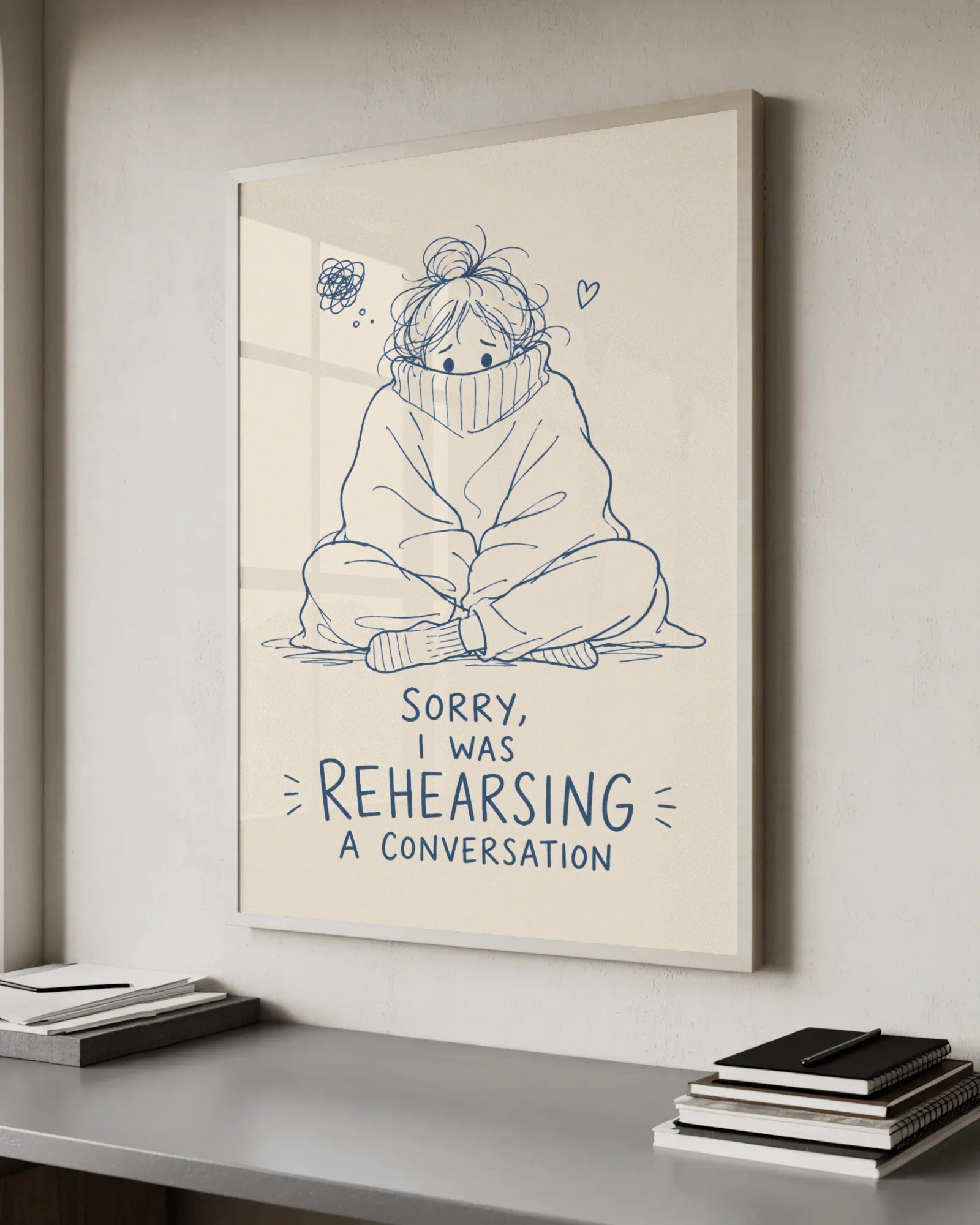 Navy continuous-line illustration on cream of an anxious person hiding in an oversized rollneck jumper, knees hugged, with the words Sorry, I was rehearsing a conversation